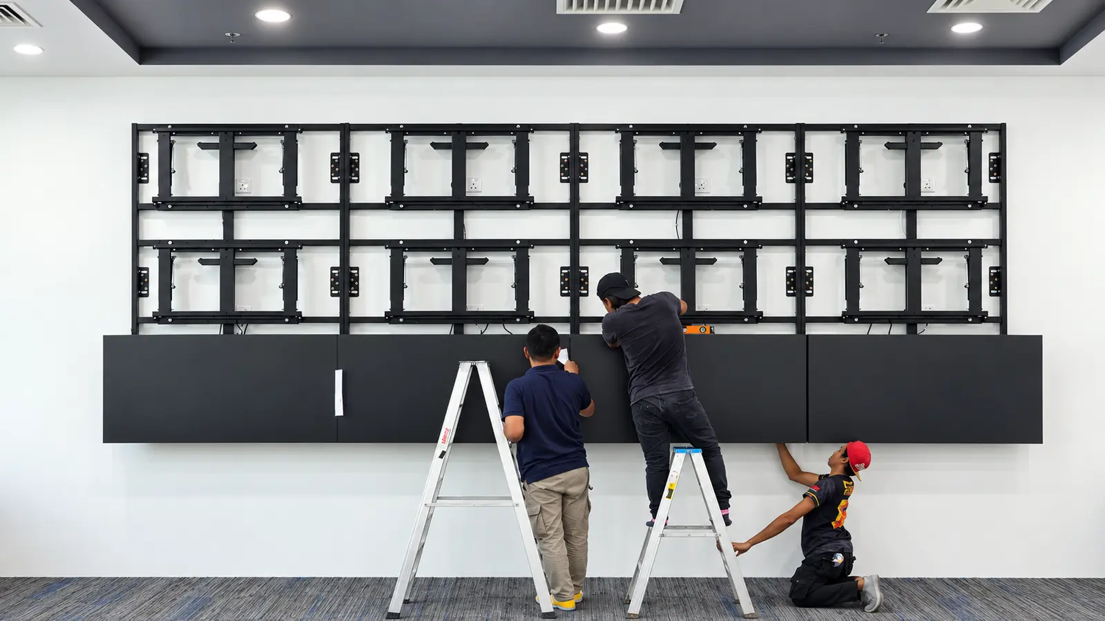 PNSS technicians installing commercial displays on a purpose-built video wall mounting structure